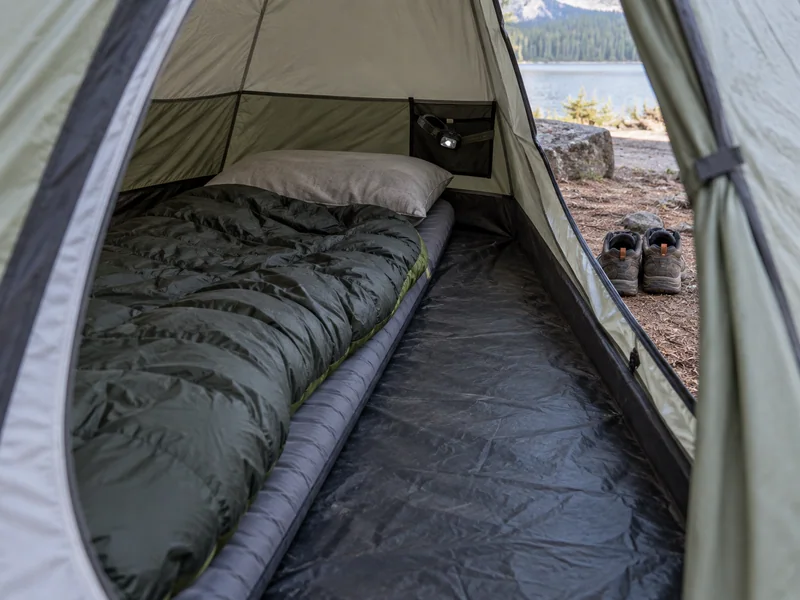 Adult sleeping bag and pillow beside a reachable headlamp with an open path to the tent door