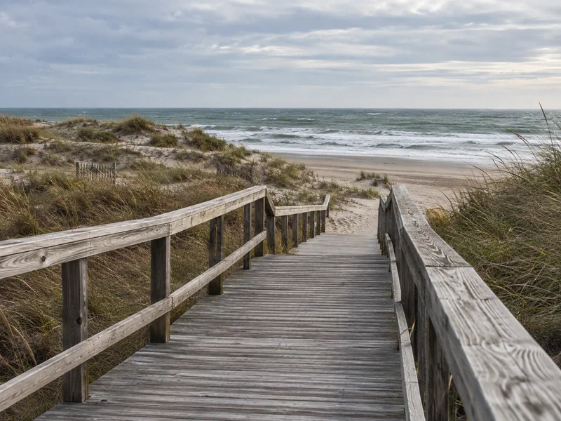 Boardwalk ending at a beach access point under an overcast coastal sky
